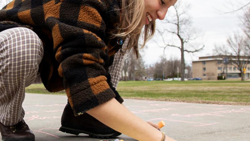 Student shading a flower on the sidewalk using chalk