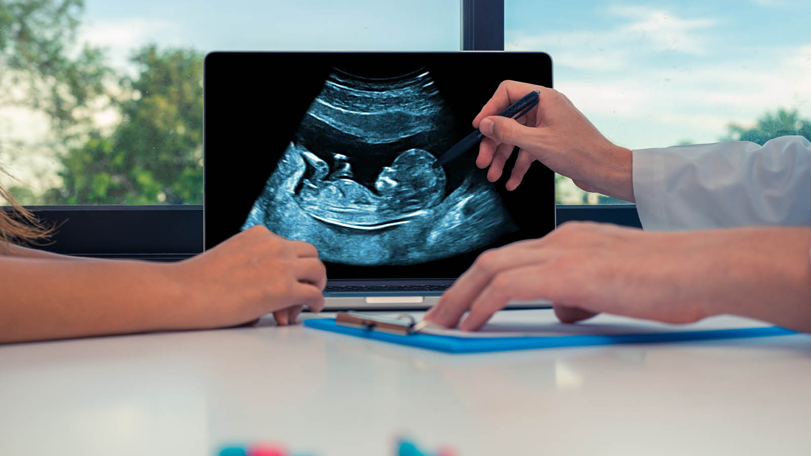 Hands at table with one pointing at an ultrasound of a fetus in a womb