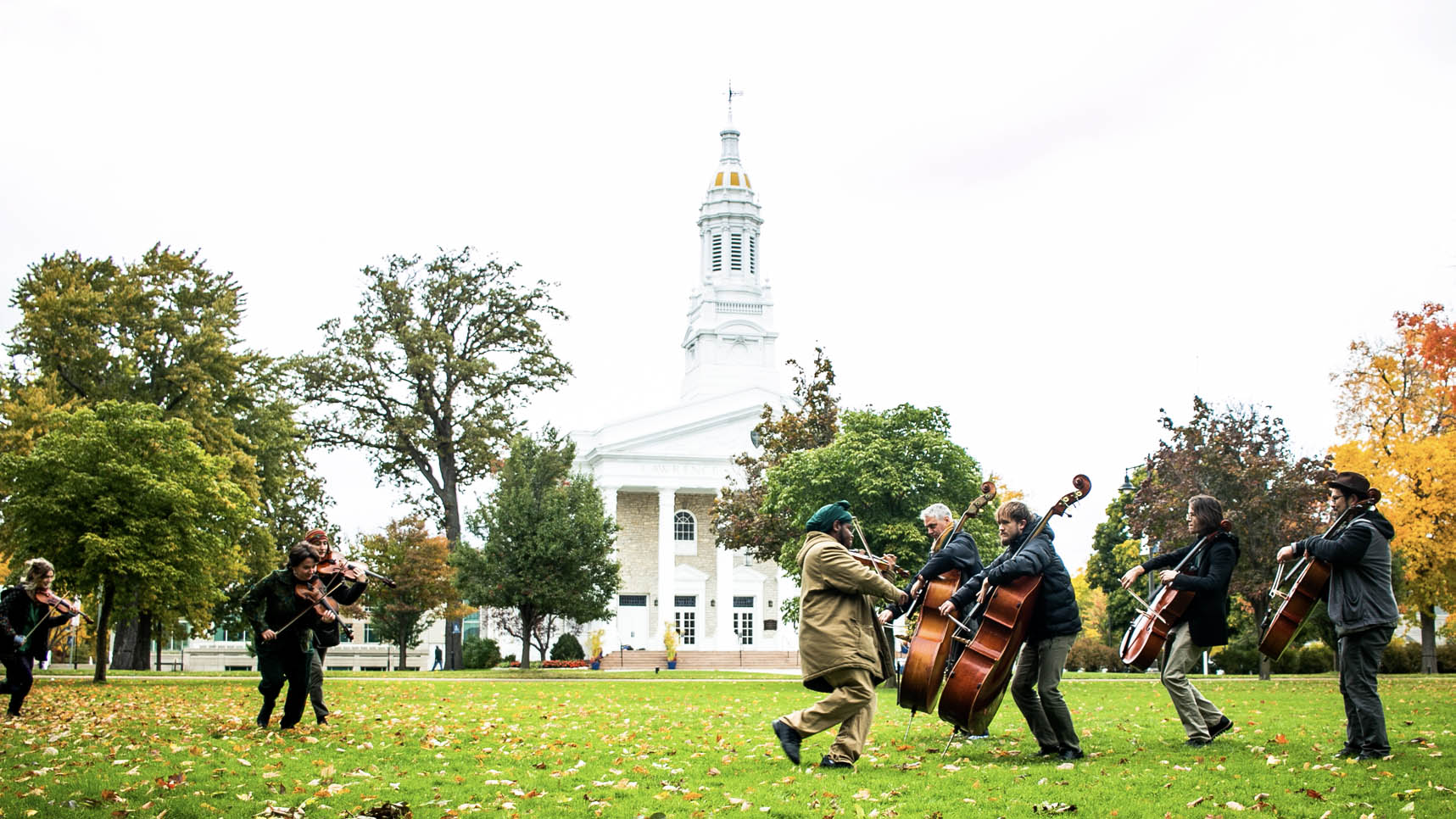 Students and faculty dancing and playing stringed instruments on Main Hall Green in the fall