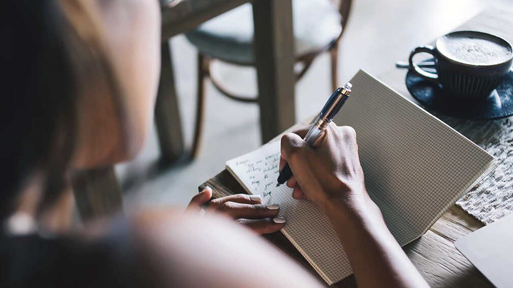 Person writing poetry in a journal at a coffee shop