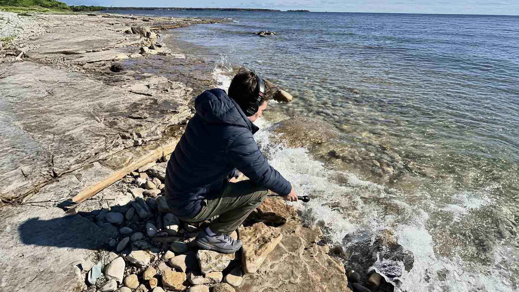 Person on lakeshore holding a microphone near the water and listening on a headset