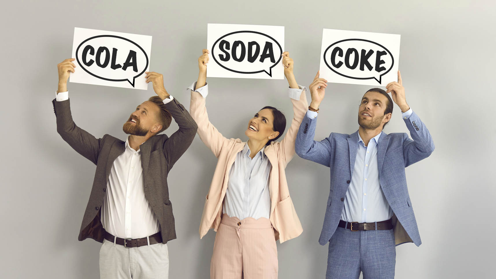 Three people holding up word bubble signs with COLA, SODA, and COKE on them