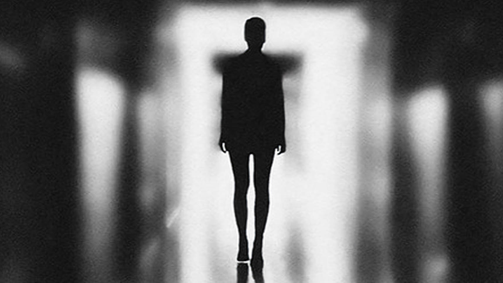 Black and white silhouette of person walking away from camera down a hall and the call is all blurry