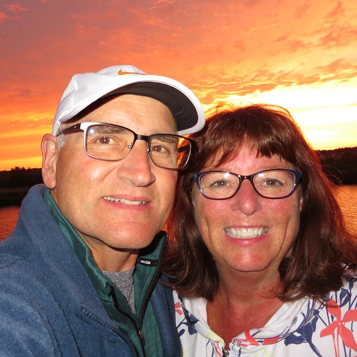Richard Zimman ’73 & Valerie Cox pose for a picture in front of a sunset.