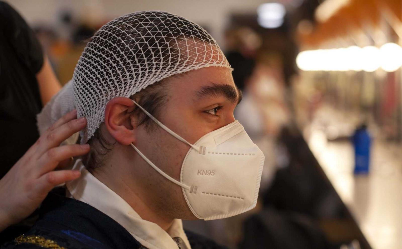 Jon Winkler, a sophomore, is fitted with a hair net as part of hair and makeup before rehearsal.