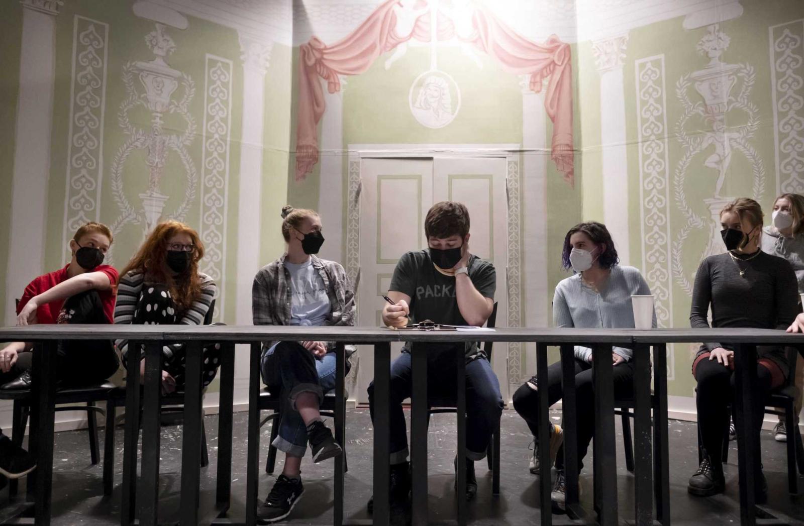 Students Maeve Shaffer, Frankie Sobel, Lexi Praxl, Alec Welhouse, Maddie Guest, Ella Rose Schaefer, and Nina Broberg sit at a table as they read a scene for Molière Inspired in the Cloak Theater.