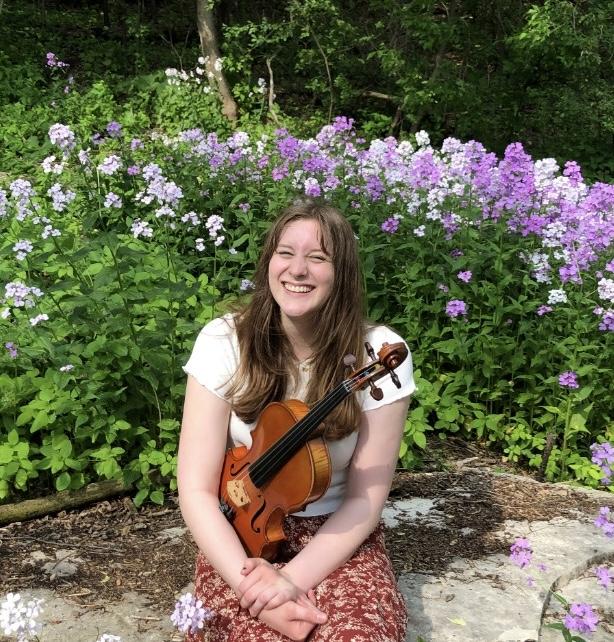 Mallory Welsch holds a violin in front of flowers.