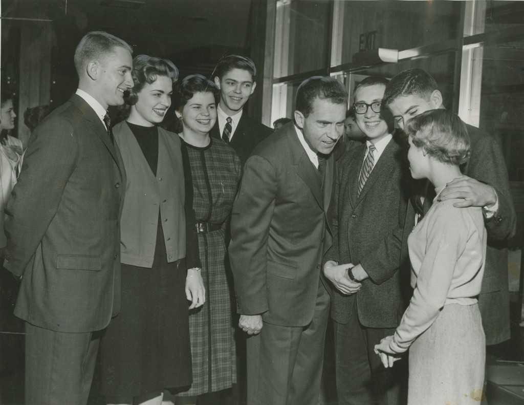Richard Nixon leans in to speak with a student in the Music-Drama Center as other students look on.