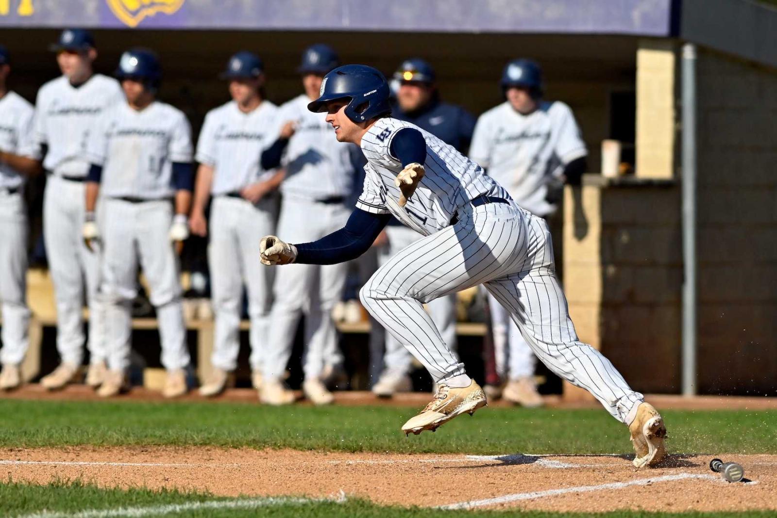 A Lawrence player sprints from the batter's box as teammates look on.