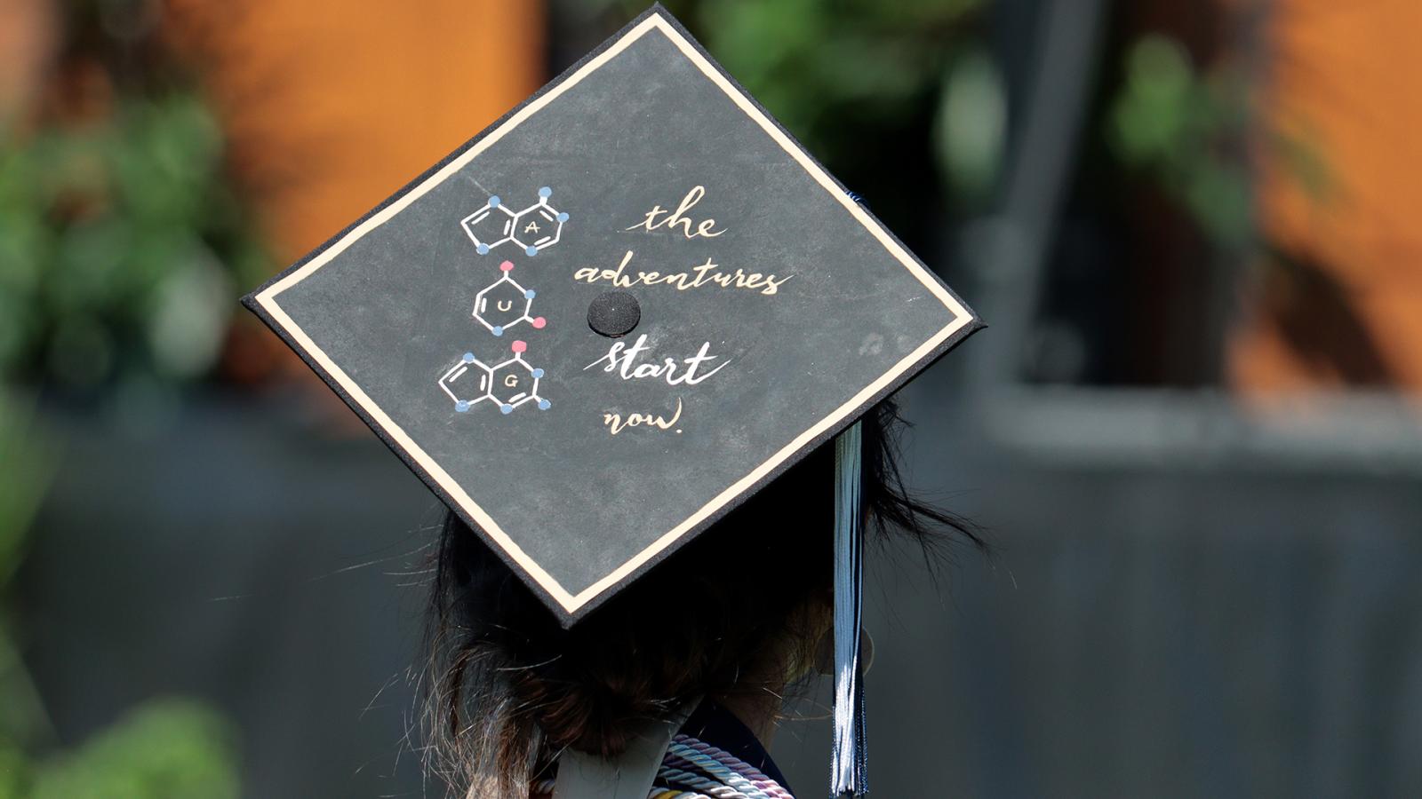Graduate with mortarboard that reads, "the adventures start now"