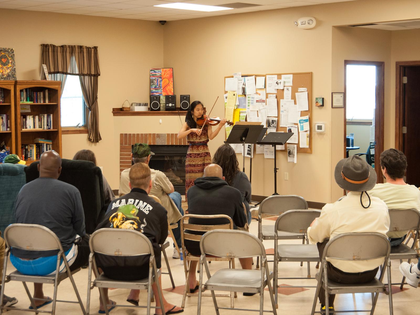 Violinist plays in a casual setting for people in folding chairs.