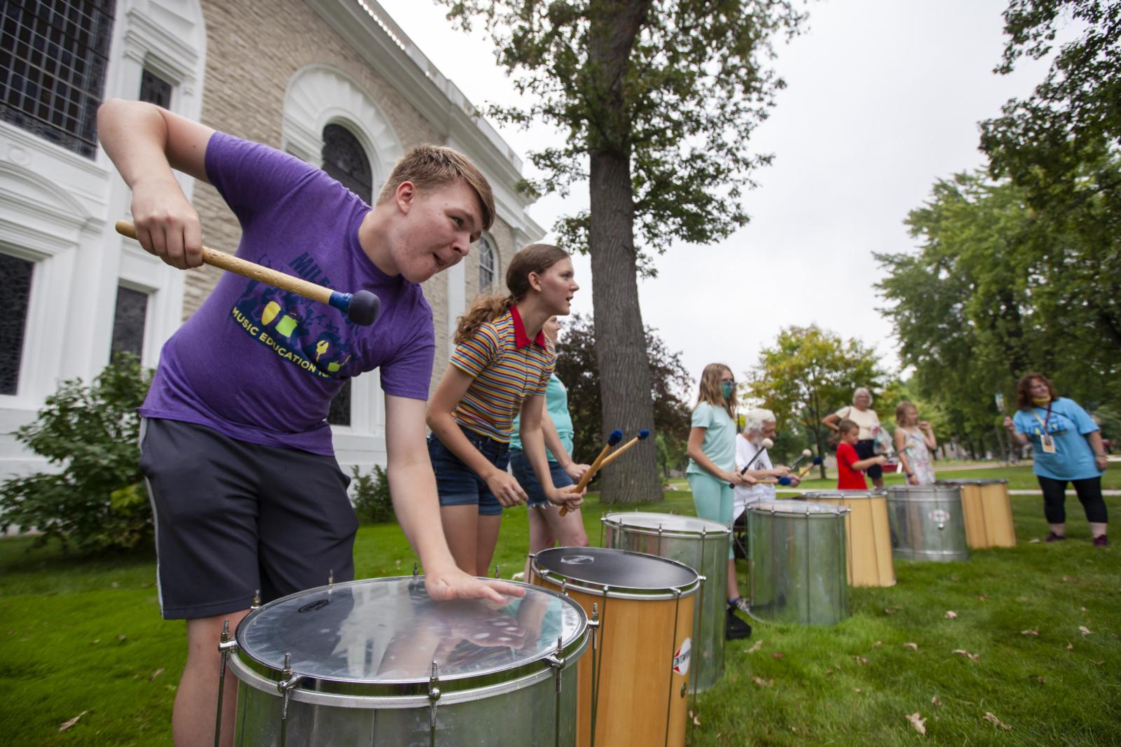 Boy plays large drum outside.