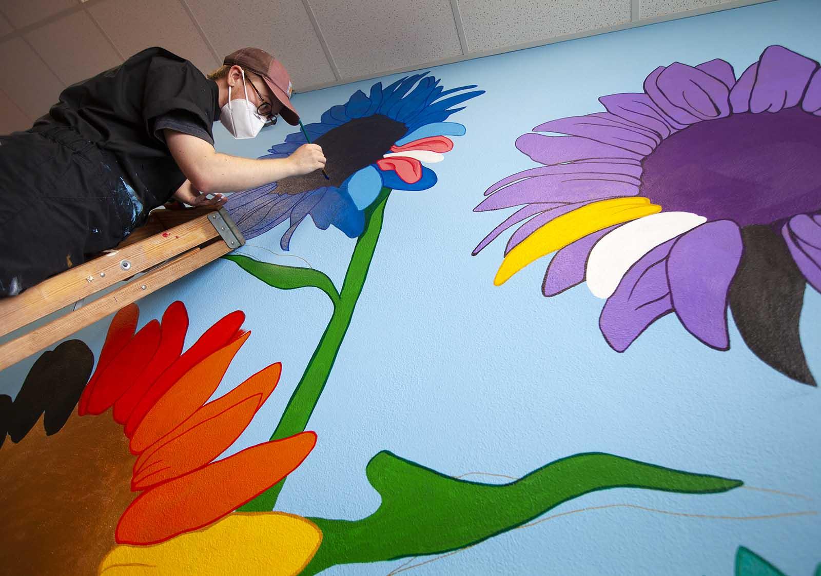 Cael Neary ’17 stands on a ladder while working on a mural in the Gender and Sexuality Diversity Center.