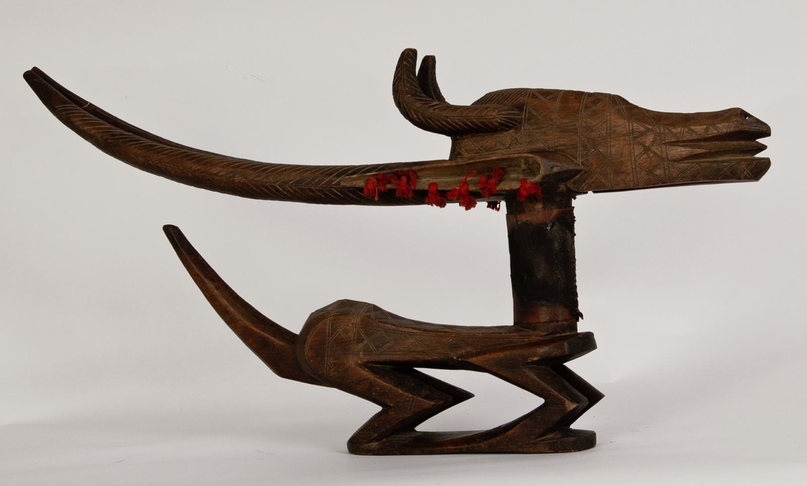 an abstracted antelope sculpture made of wood with red string knots in its ear, seen from the right side