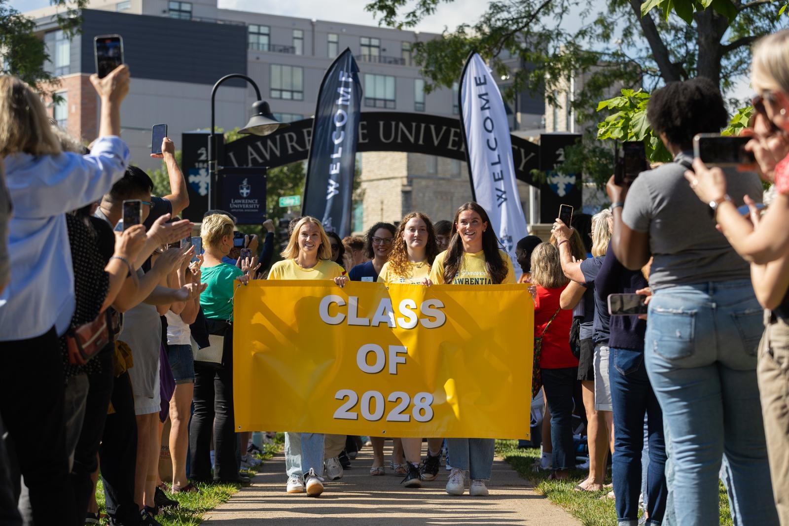 New students carry the Class of 2028 banner as they walk through the Lawrence Arch.