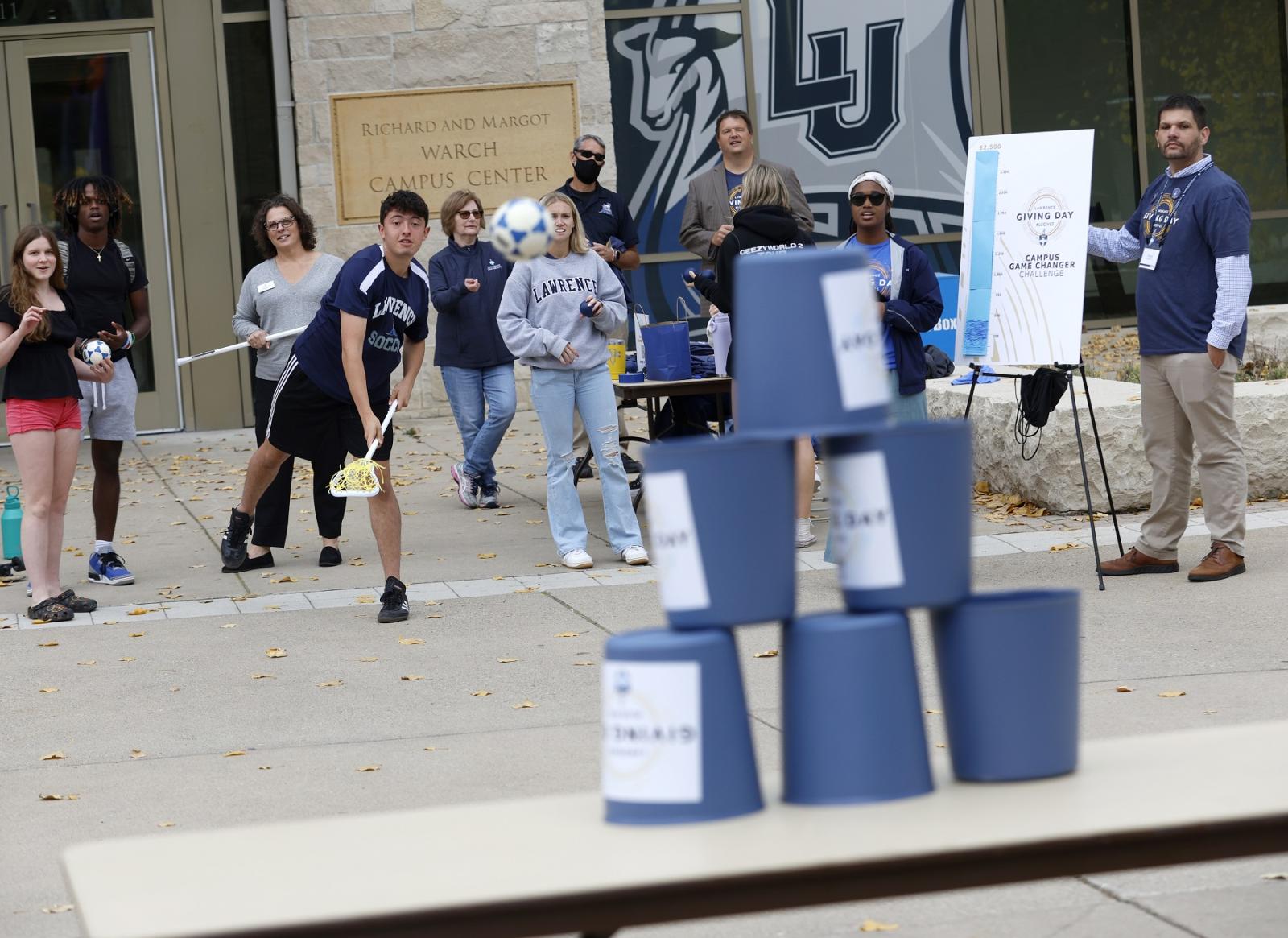 Students use lacrosse sticks to knock down cups to win prizes during Giving Day activities outside of Warch Center.