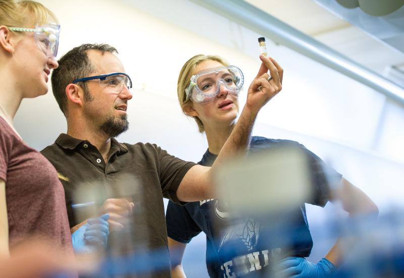 Stefan Debbert Chemistry Profile image with two students in lab they are wearing safety glasses and looking at a caped vile of solution