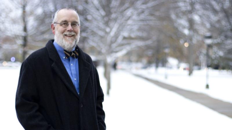 Tim Spurgin, wearing a bow tie and dark coat, smiles at the camera on a snowy Main Hall Green.