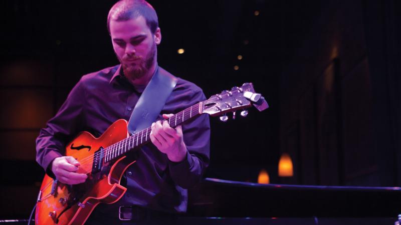 Student playing guitar on stage