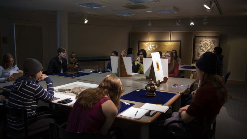 East Asian History students sitting around square tables studying historical artifacts and artwork