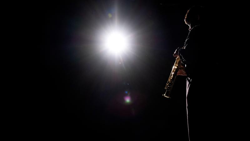 Student plays intrument on dark stage. Spot light is shining