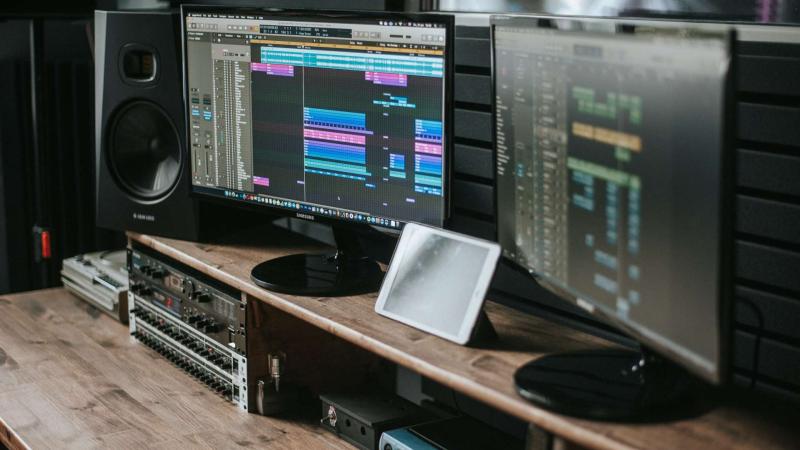 two monitors displaying music editing software sits on a table, with a speak on either side of them