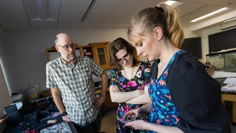 Jeff Clark and Kat McClain look on as Sydney Closson works through the wiring of a spectrometer. 