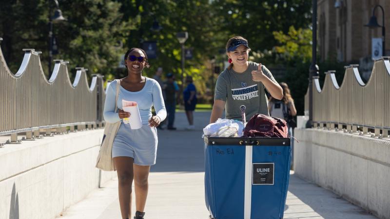 A student pushes a cart across the walking bridge on move-in day.