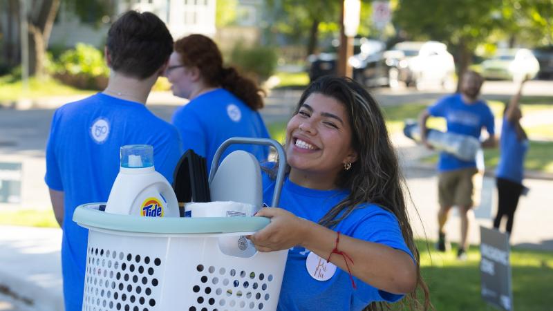 A student carries a laundry basket into a residence hall during move-in.