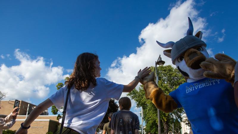 The mascot Blu high-fives a student during the walk to the President's Welcome.