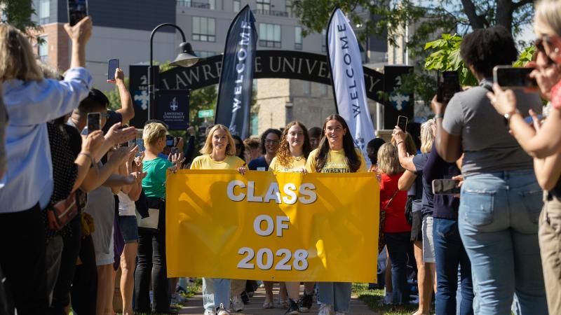 New students carry the Class of 2028 banner as they walk through the Lawrence Arch.