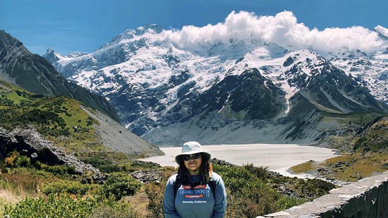 Naomi Torres-Solorio stands in front of a scenic backdrop with a lake and mountains.