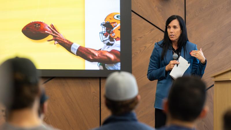 Gabrielle Valdez Dow speaks to the class of Sport Management at the Business and Entrepreneurship Center in Fox Commons. An image behind her shows a Packers player.