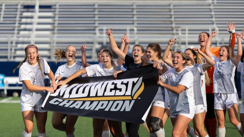 Women's soccer players celebrate with a Midwest Conference Champion banner.