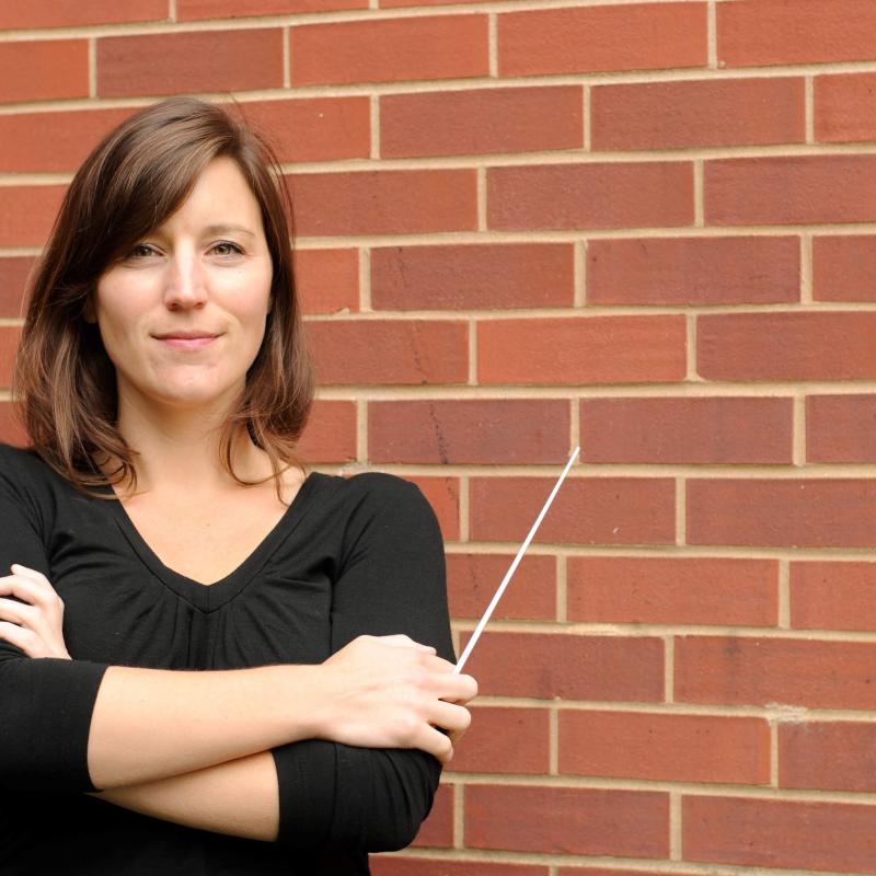 Photo of Dr. Gravelle, holding a baton and in front of a red brick wall.