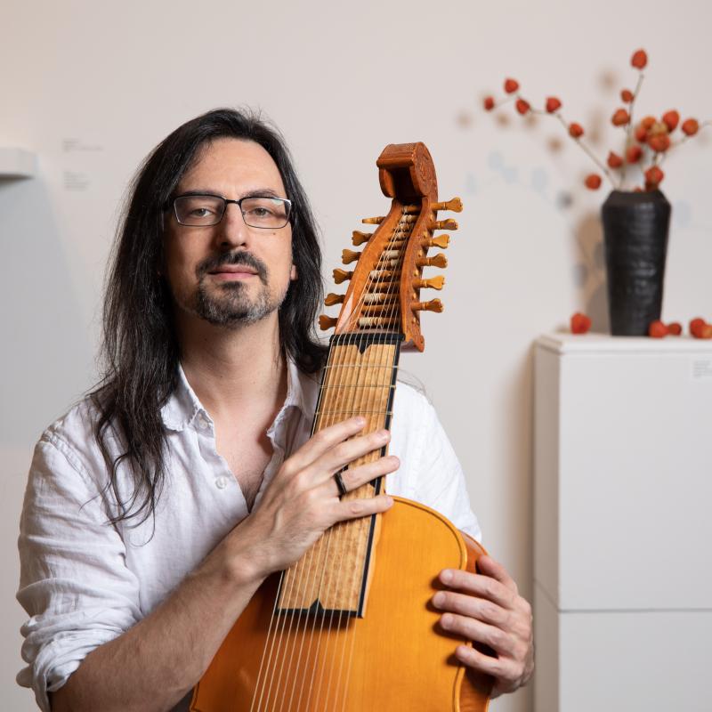 Long-haired man holding a lirone (a 12-stringed baroque instrument). 