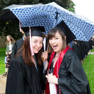 Two Lawrentians smiling in cap and gown, stand under a polka dotted umbrella.