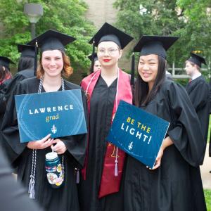 Two graduates hold signs that say "Lawrence grad" and "Be the light!"