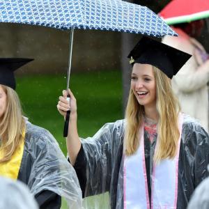 Graduate holding umbrella, laughing, during processions.