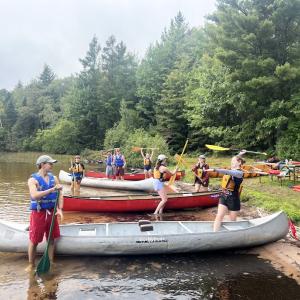 Group shot of students standing by canoes on the lake shore - 2024 Land and Sea Pre-orientation Experience