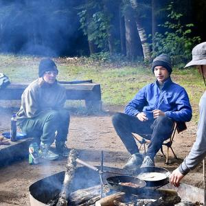 Students sitting by the fire and cooking food - 2024 Land and Sea Pre-orientation Experience