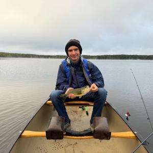 Student sitting in a canoe and holding a bass he caught while fishing - 2024 Land and Sea Pre-orientation Experience