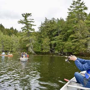 Student fishing while others canoe nearby - 2024 Land and Sea Pre-orientation Experience